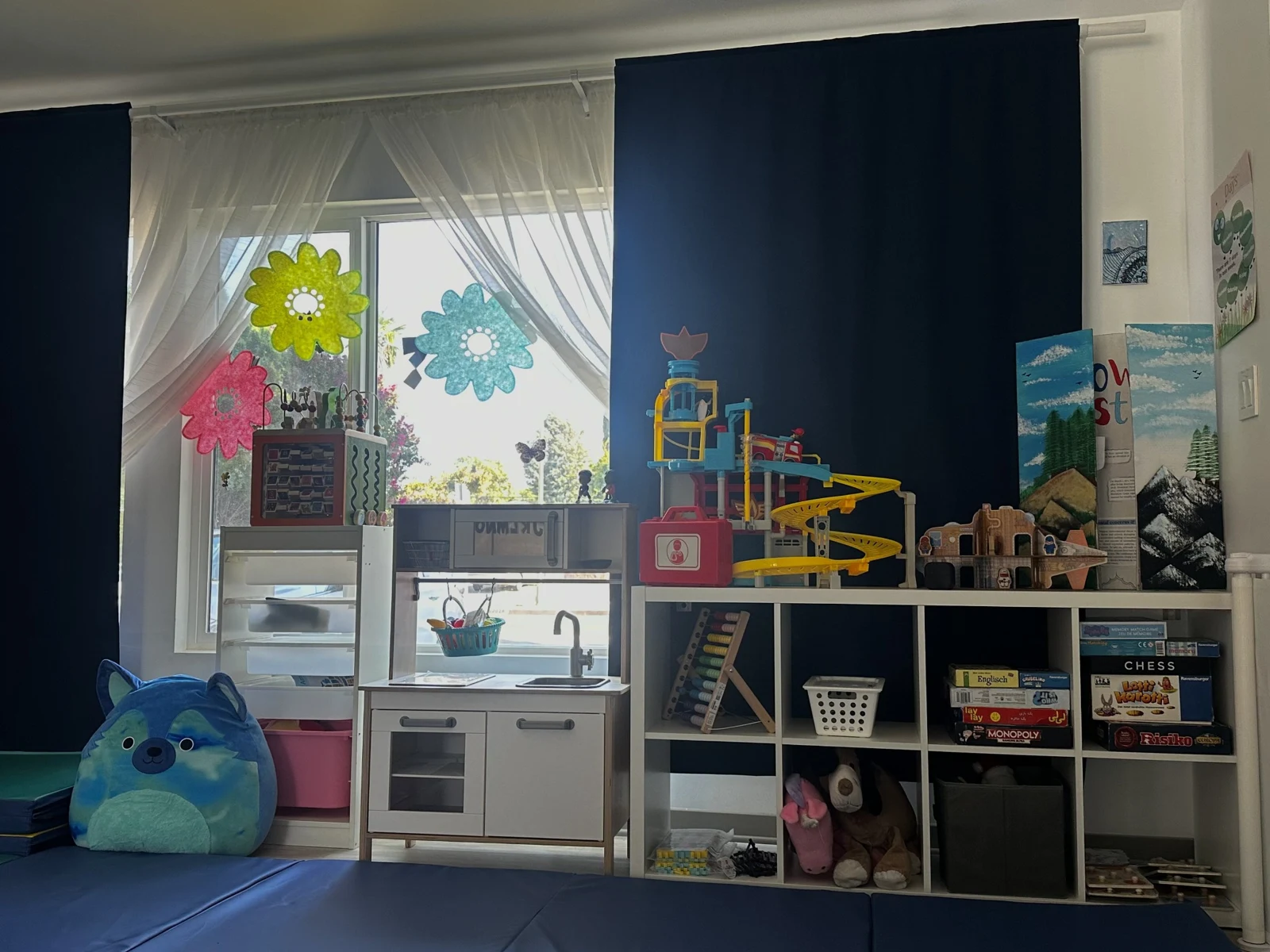 Toy kitchen, play sets, and books beside a sunny classroom window